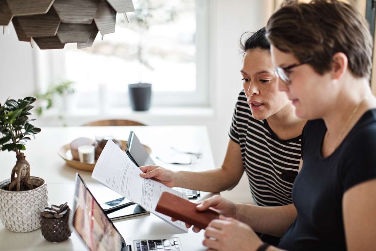 Två kvinnor sitter vid ett matbord och arbetar med pappersarbete framför en laptop